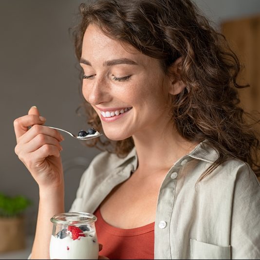 Ein Frau löffelt lächelnd einen Joghurt mit Beeren.