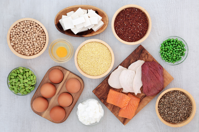 Ausschnitt von einem Tisch mit eiweißreichen Lebensmitteln: Edamame, Kichererbsen, Tofu, Quinoa, Hirse, Erbsen, Linsen, Fleisch, Fisch, Quark und Eier.