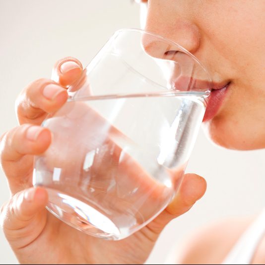 Eine Frau, die aus einem Wasserglas trinkt.