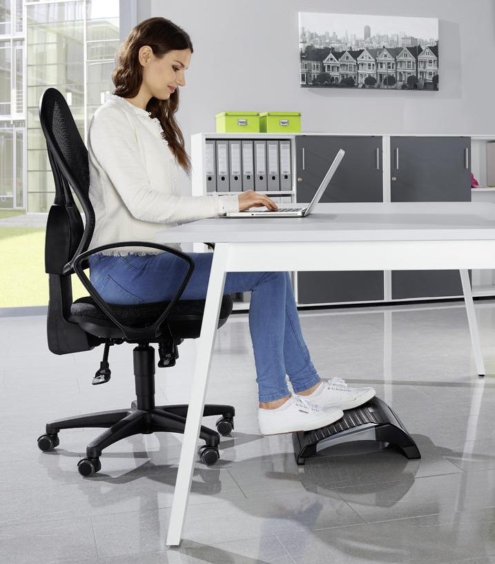 Eine Frau sitzt an einem Schreibtisch und hat ihre Füße auf einer Fußstütze abgestellt.