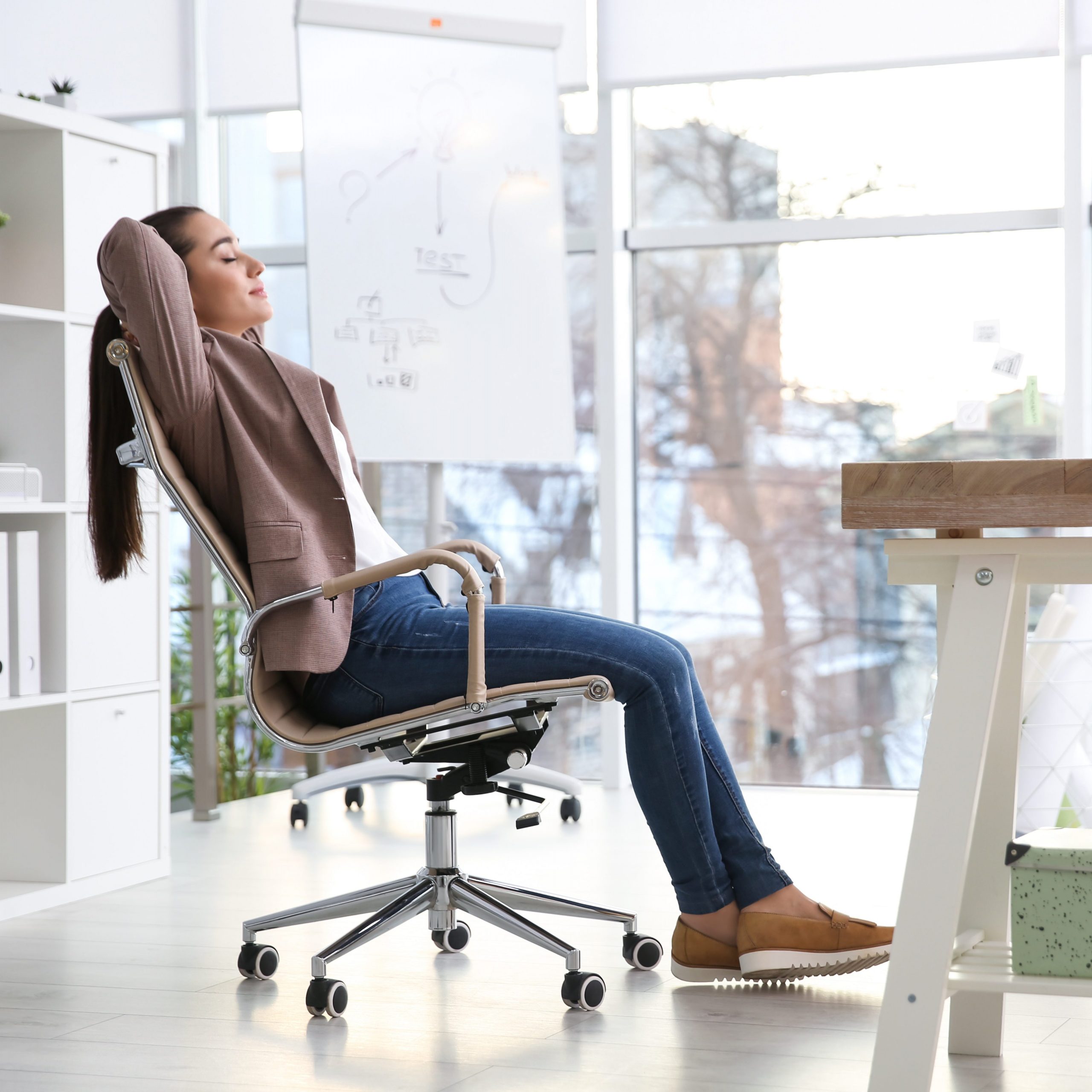 Eine Frau lehnt sich mit geschlossenen Augen entspannt ih ihrem Bürostuhl zurück.