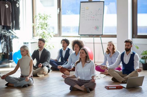 Eine Gruppe von Businessleuten sitzt auf dem Boden und meditiert. Dahinter steht ein Flipchart mit einem Diagramm.
