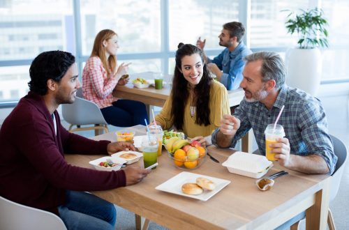 Arbeitskollegen verbringen gemeinsam ihre Pause in der Kantine und trinken Smoothies und essen ihr Mittagessen.